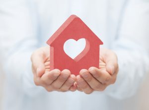Hands holding a red house cutout with a heart symbol, representing love and care.